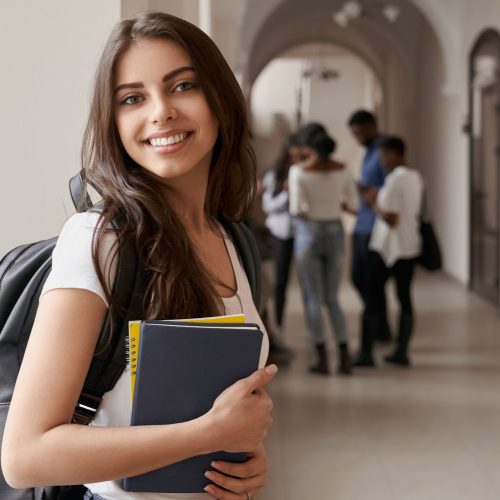 A smiling young woman with a backpack holding textbooks,