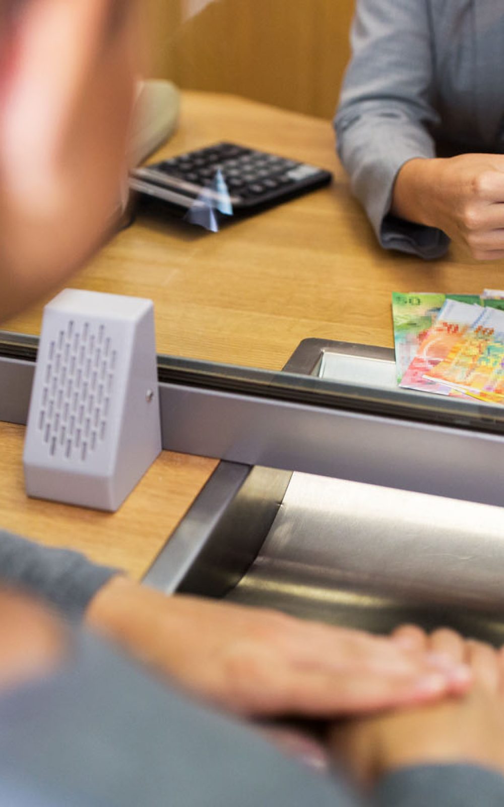 A close-up scene at a bank counter with a customer and a teller,