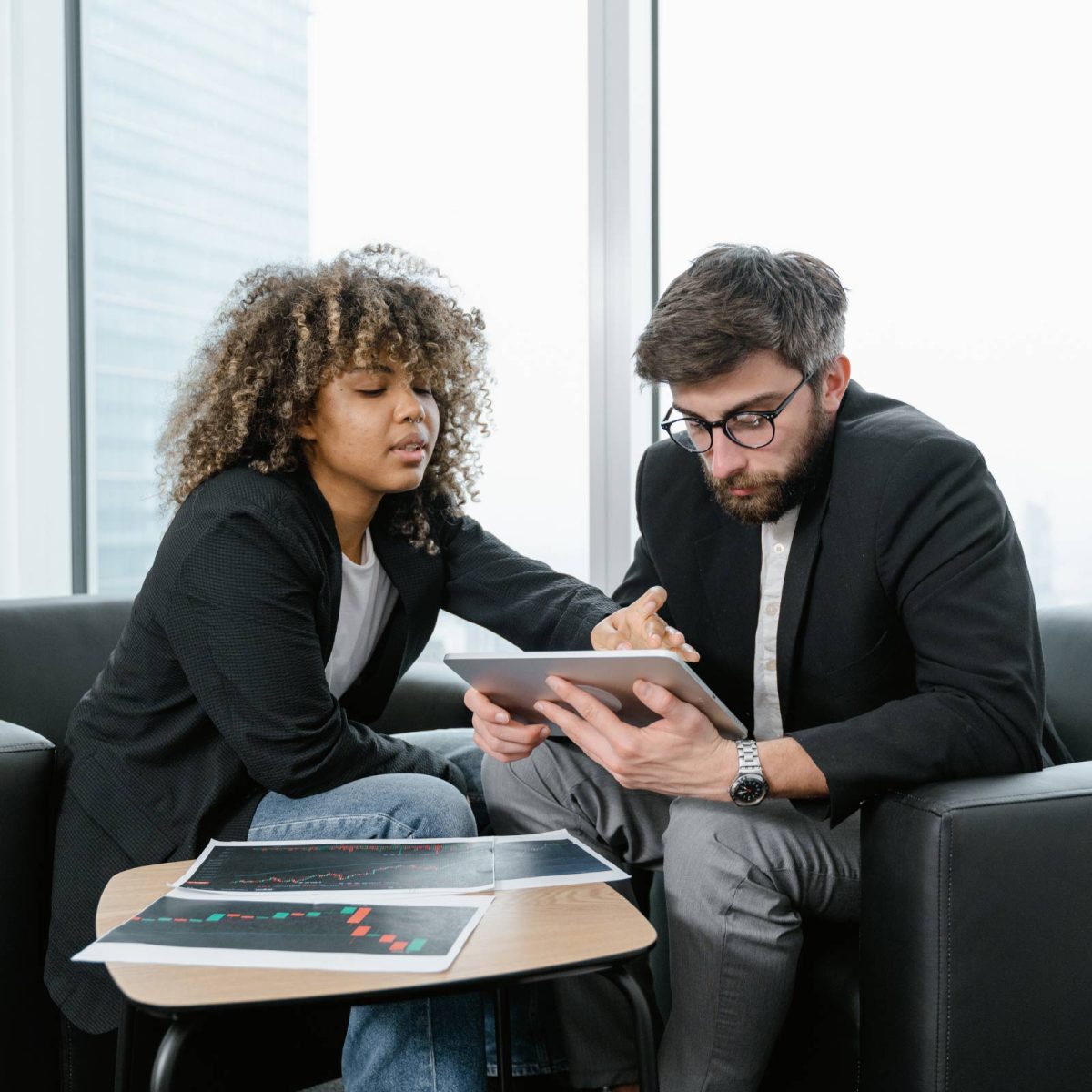 Two professionals engaged in a serious discussion over a digital tablet - Moneyroyalexchange